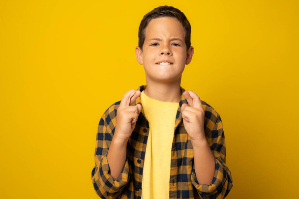 Schöner kleiner Junge in lässigem Hemd, der vor isoliertem gelben Hintergrund steht und mit erhobenem Zeigefinger lächelnd vor Hoffnung gestikuliert. Glück und abergläubisches Konzept. - Foto, Bild