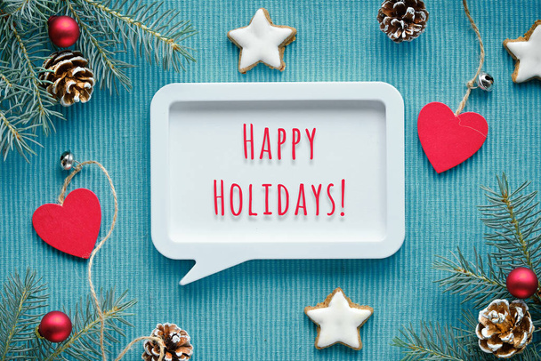 Text Happy Holidays in speech bubble frame. Christmas simple minimal background with fir twigs, candy canes, pine cones, star cookies. Merry Xmas, Happy Holidays. Flat lay, top view on turquoise wood. - Photo, Image