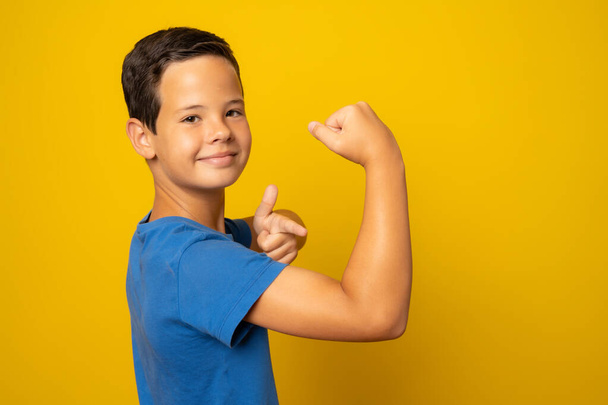 Vahva poika osoittaa lihaksia, eristetty keltaisella pohjalla - Valokuva, kuva