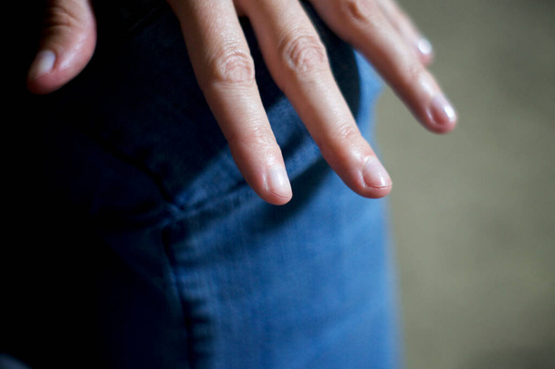 Close up with shallow depth of field a woman's hand is resting on her jean clad knee with fingers extended - Fotoğraf, Görsel