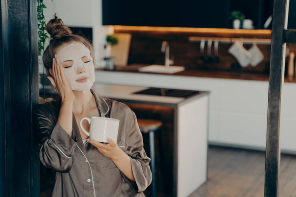 Mladá žena v hedvábném pyžamu zůstat doma a užívat si ranní šálek kávy - Fotografie, Obrázek