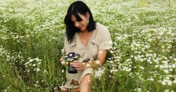 Vrouwelijke fotograaf zittend op bloemenveld landschap en op zoek foto op camera - Video