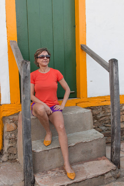 Señora sentada en los pasos contra un fondo verde con ajuste amarillo y zapatos a juego - Foto, imagen