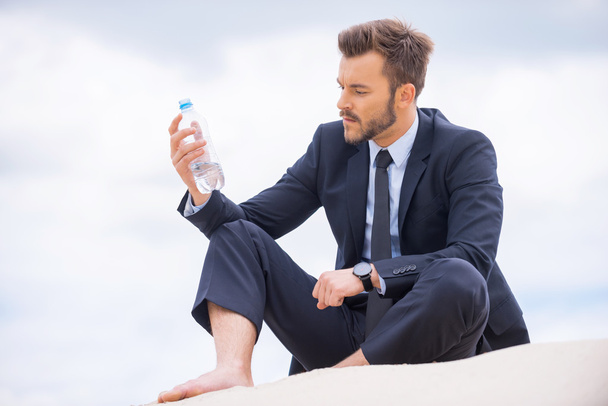 Depressed young businessman holding bottle with water - 写真・画像