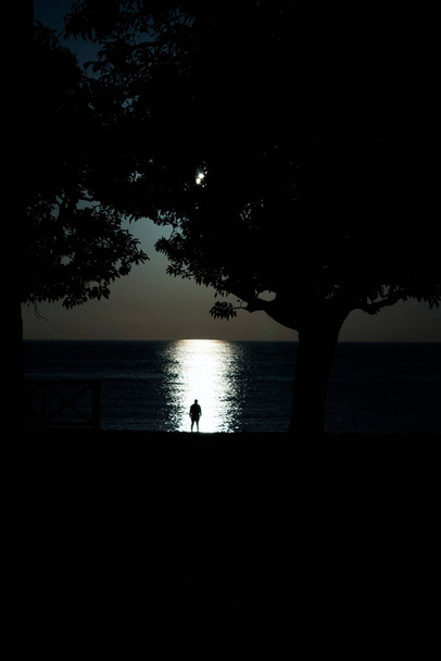 silueta muže proti moři za soumraku s odlesky ve vodě - Fotografie, Obrázek