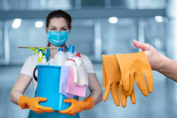 Servicios de limpieza locales industriales. La señora de la limpieza muestra guantes de goma sobre un fondo borroso. - Foto, imagen