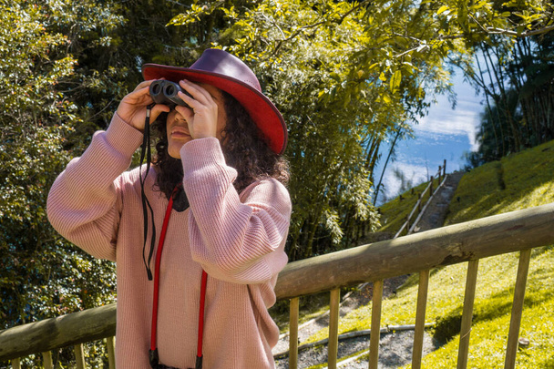 Mujer joven con pelo rizado y sombrero observando pájaros con prismáticos - Foto, imagen