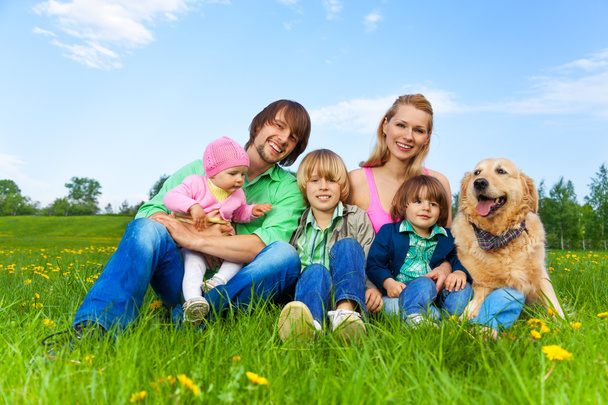 Smiling family sitting on green grass with dog - Fotó, kép