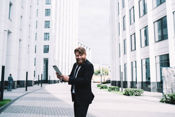 Laughing male employee with tablet looking at the camera while standing next to stylish office after successful meeting at work - Φωτογραφία, εικόνα