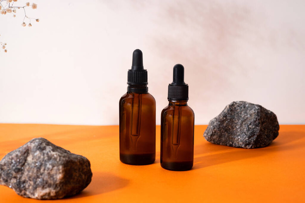 Brown serum or oil glass mock up bottle with pipette over orange background with dried flower and wooden forms. Concept of natural organic cosmetic, cosmetology, dermatology. - Photo, Image