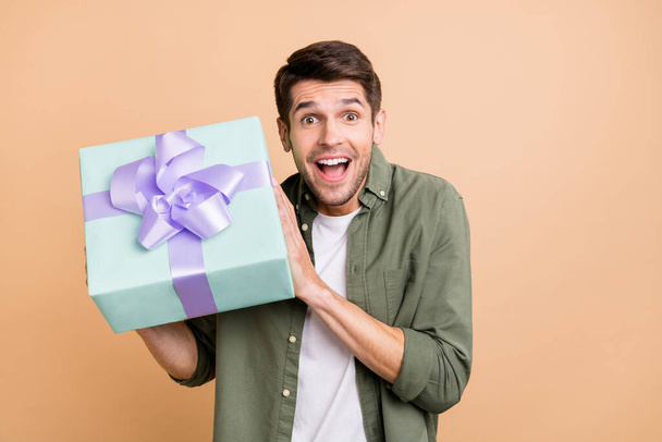 Photo of amazed charming happy young man hold hands gift curious present isolated on beige color background - Photo, image