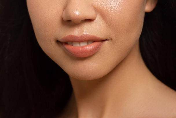 Крупним планом жіночі губи з модним натуральним бежевим макіяжем для губ. Макро сексуальний блідий макіяж для губ. Ніжна чиста шкіра і хвилясте волосся брюнетки. Косметологія, СПА, збільшення губ
 - Фото, зображення