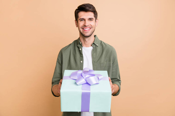 Photo of charming happy young man give gift box you smile celebrate holiday isolated on beige color background - Foto, immagini