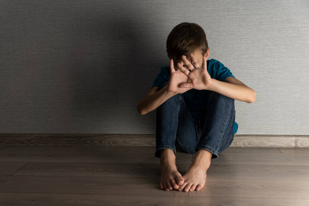 Pelokas poika sulkee päänsä ja kasvonsa käsillään piiloutuen väärinkäytöltä. Kotiväkivalta, emotionaalinen trauma onnettomassa lapsuudessa. - Valokuva, kuva