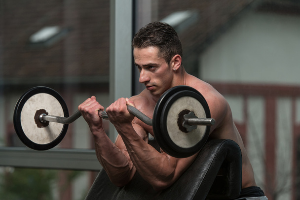 Bodybuilder Performing Biceps Curls With A Barbell - Фото, изображение