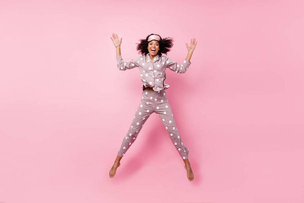 Photo of adorable funny curly dark skin woman dotted nightwear rising arms hands jumping high isolated pink color background - Фото, зображення