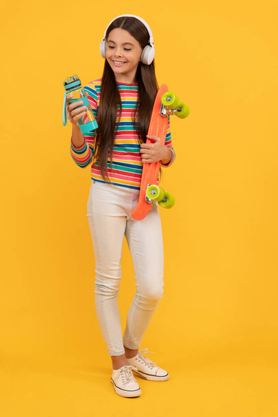 щаслива дівчина-підліток скейтбордист слухати музику в навушниках з дошкою пенні і водою, ковзаняр
. - Фото, зображення