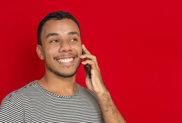 un hombre sonriendo usando un teléfono celular con un fondo rojo - Foto, imagen