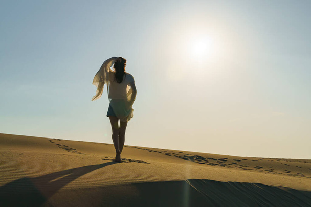 Millennial Woman standing on wavy sand dunes in desert landscape at golden sunset light and wind. - Fotó, kép