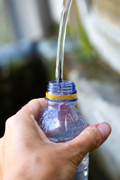 femmes caucasiennes main avec bouteille en plastique blu. Fille remplit une bouteille d'eau fraîche pure dans une journée d'été. Fontaine extérieure d'eau potable. Concept d'approvisionnement et de distribution d'eau.  - Photo, image
