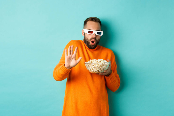 Imagen del hombre en gafas 3D viendo películas, asustándose de los efectos especiales, mirando con asombro, de pie con palomitas de maíz sobre fondo blanco - Foto, Imagen