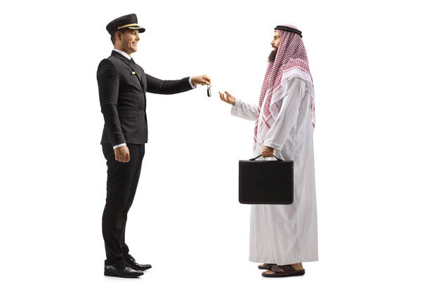 Full length profile shot of a chauffeur giving car keys to a saudi arab man isolated on white background - 写真・画像