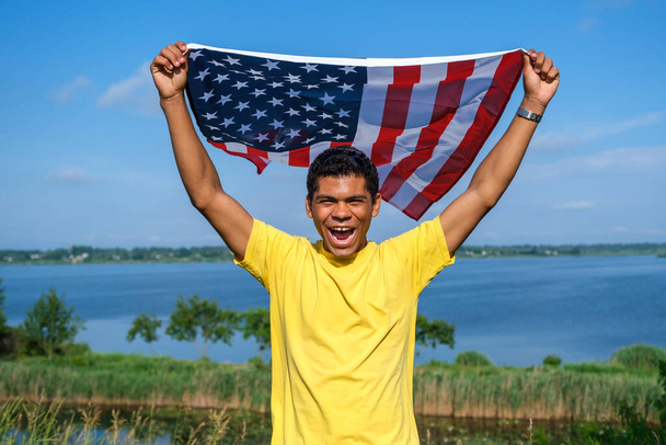 Ο άνθρωπος κοιτάζοντας κάμερα και περήφανα κρατώντας αμερικανική σημαία στην αγκαλιά του - Φωτογραφία, εικόνα