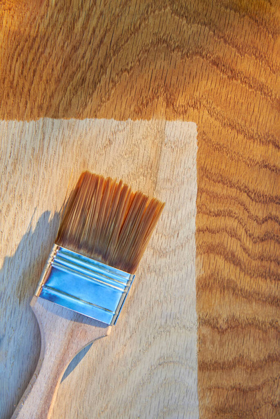 Ζωγραφική ξύλινη επιφάνεια με βερνίκι, πινέλο σε ξύλο δρυός, πάνω όψη, αντιγραφή χώρου. - Φωτογραφία, εικόνα