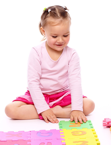 Cute little girl is playing with alphabet while sitting on floor, isolated over white - Φωτογραφία, εικόνα
