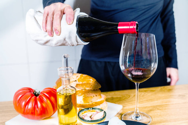 典型的なスペイン料理やカタログ料理で赤ワインを提供する匿名の人。トマトとパン,イベリアハム,ヤギチーズ,油とニンニク.木製の背景に夕食やタパスを準備する. - 写真・画像