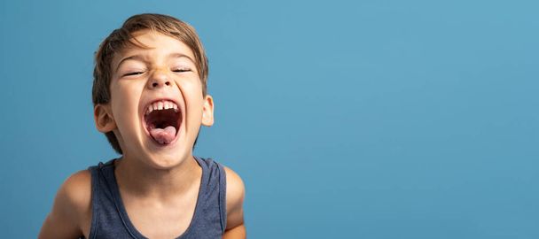 Vista frontale del piccolo ragazzo caucasico di quattro anni in piedi di fronte allo studio di sfondo blu girato bambino giocoso rendendo volti felicità e concetto di gioia - Foto, immagini