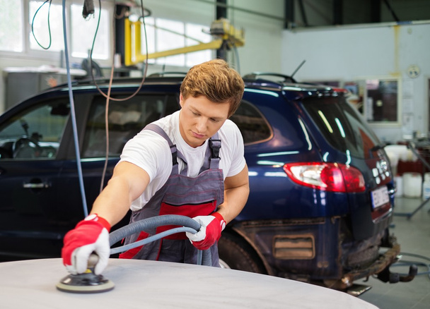 Young serviceman performing grinding with machine on a car bonnet in a workshop - Foto, Imagem