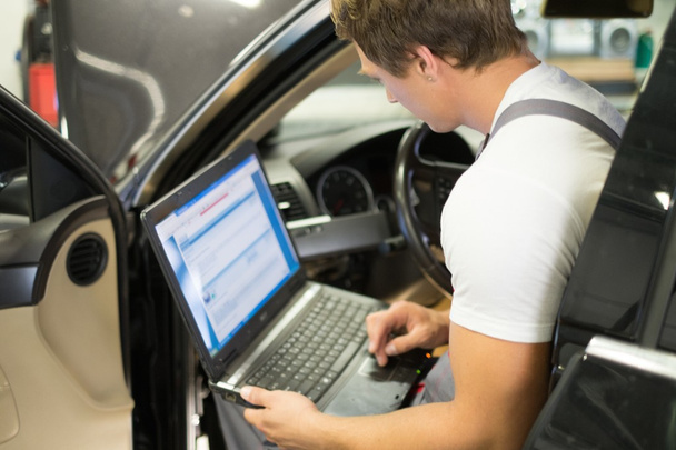 Serviceman faire des diagnostics de voiture avec ordinateur portable dans un atelier
 - Photo, image