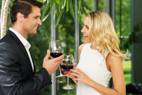 Fröhliches Paar mit Rotweingläsern im Gespräch - Foto, Bild