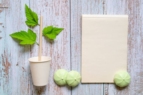 Бумажная чашка с соломой с зелеными листьями, блокнот и сладости, копировальное место, нулевые отходы. Высокое качество фото - Фото, изображение
