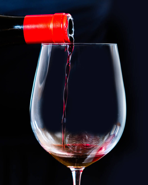 Sommelier serveert Spaanse zwarte wijn in een elegante kristallen beker met een zwarte achtergrond. Giet rode wijn uit de fles in het wijnglas op zwart. - Foto, afbeelding
