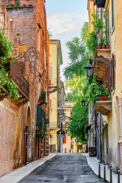 View of narrow street at historic centre of Verona, Italy. Facades of houses in morning sun. Verona is a popular tourist destination of Europe. - Valokuva, kuva