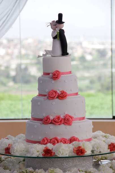 Torta de matrimonio de color blanco con decoracion de flores comestibles, en la parte de arriba se puede ver la representacion de los recien casados. Wyobraź sobie idealny para promocionar pasteleria. - Zdjęcie, obraz