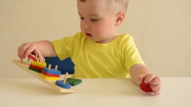 niño pequeño juega constructor mientras está sentado en una mesa blanca. juego educativo Montessori habilidades motoras finas. concepto de desarrollo temprano - Metraje, vídeo