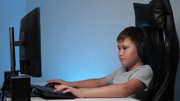 Chłopiec ze słuchawkami bawiącymi się na komputerze - Materiał filmowy, wideo