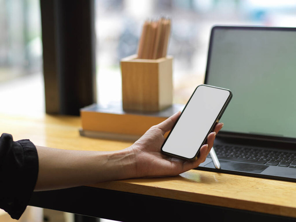 Женщина держит в руках смартфон и открывает ноутбук с пустым экраном для рекламы бренда, деловая женщина пишет смс на мобильный телефон во время работы на планшете  - Фото, изображение