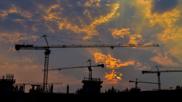 tijd lapse zonsondergang en silhouet kraan werken in grote bouwplaats - Video
