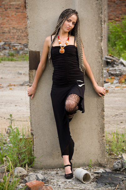 Fashionable girl in black dress alongside of column on the dirty industrial place - Fotó, kép