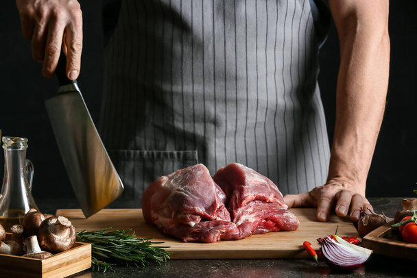 Чоловік з сирим свинячим м'ясом і овочами на темному столі
 - Фото, зображення