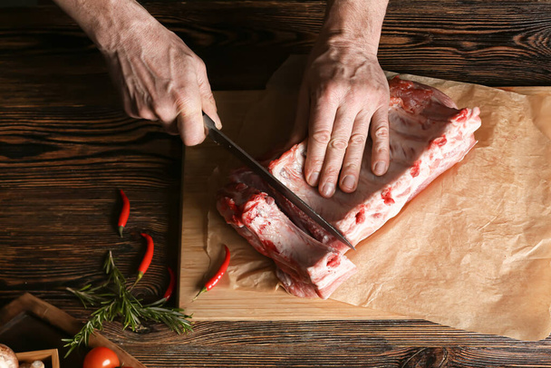 Hombre cortando costillas de cerdo crudas en mesa de madera - Foto, Imagen