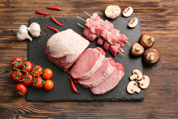 Płyta łupkowa z surowego mięsa wieprzowego, przypraw i warzyw na drewnianym tle - Zdjęcie, obraz