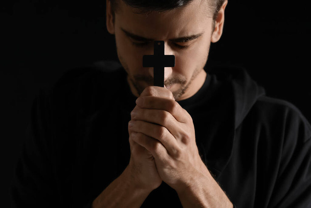 Religiöser junger Mann mit Kreuz betet auf dunklem Hintergrund, Nahaufnahme - Foto, Bild