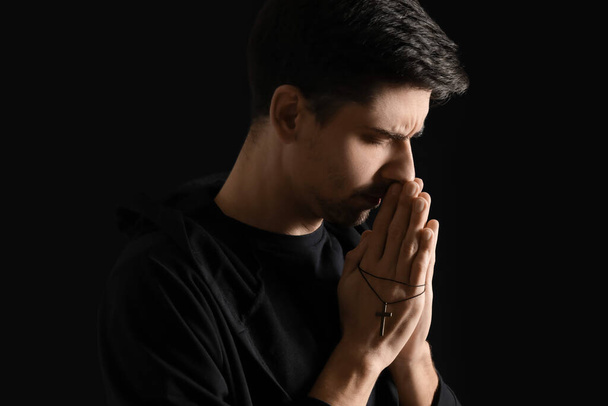 Religijny młody człowiek z krzyżem modlący się na ciemnym tle - Zdjęcie, obraz