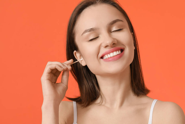 Young woman cleaning ears with cotton bud on color background - Foto, Bild