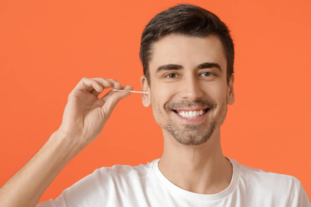 Young man cleaning ears with cotton bud on color background - Foto, Imagen